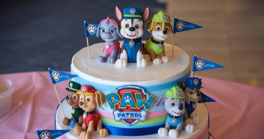 Edible Paw Patrol decorations including figurines, paw-print stencils, and colorful sprinkles on a wooden table.